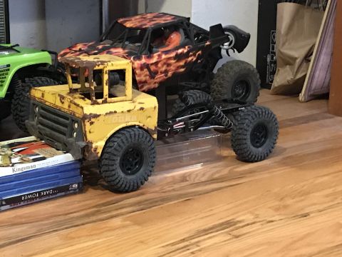 1989 Ford Bronco - Two toy trucks, one yellow and one with a flame design, are positioned on a wooden floor.