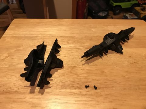 1989 Ford Bronco - Two black plastic parts, likely from an RC car axle assembly, are laid out on a wooden table. One part is a complete axle housing, while th…