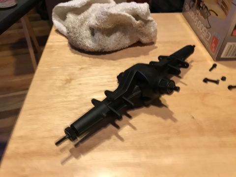 1989 Ford Bronco - A black differential housing part is laid out on a wooden table next to a white cloth and a box with some text on it.