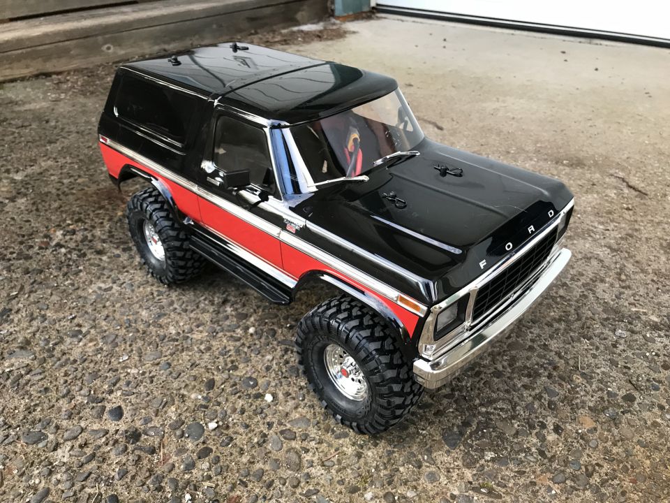 Black and red 1980s Ford Bronco RC truck with chrome details and off-road tires on gravel.