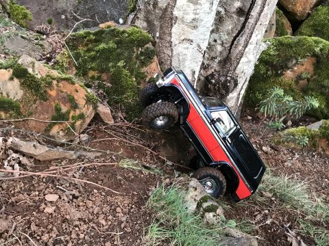 1989 Ford Bronco - RC rock crawler truck navigating a difficult, rocky, and wooded terrain.