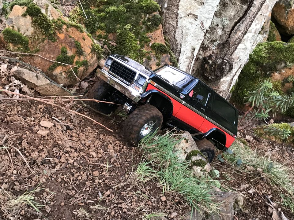Black and red RC SUV climbing over rocks and dirt.