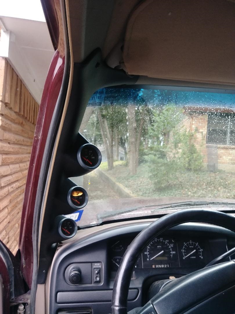 Interior view of a vehicle dashboard with three gauges on the A-pillar and steering wheel.