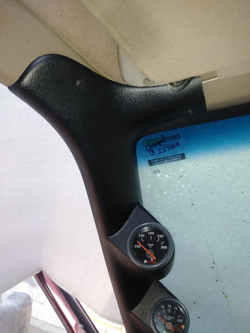 Black A-pillar gauge pod with temperature and oil pressure gauges inside a vehicle.