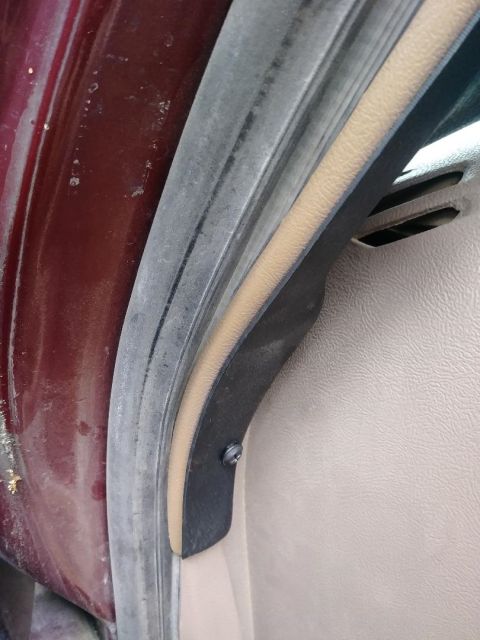 1996 Ford Bronco - Close-up view of the weather stripping and interior trim on a vehicle door jamb. A black screw secures a piece of black trim to the interio…