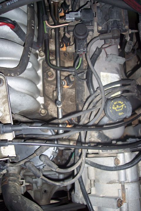 1995 Ford Bronco - This is a close-up, angled view of the engine bay of a 1995 Ford Bronco, focusing on the fuel injectors, wiring harnesses, and the oil cap.…