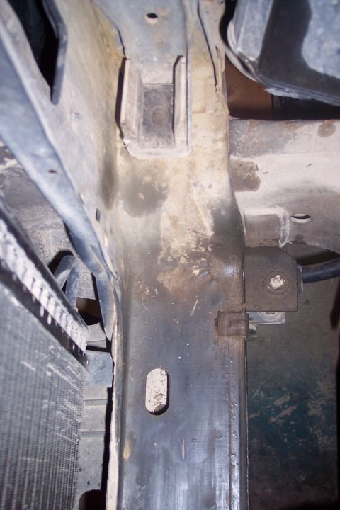 1995 Ford Bronco - This image shows the underside of a vehicle's frame, likely near the radiator support. Visible components include rusted metal brackets, a…