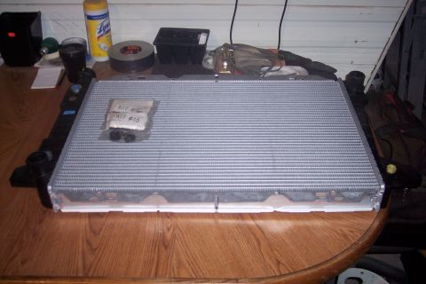 1995 Ford Bronco - A new aluminum radiator with two small plastic kits labeled "KIT #" and "KIT # 15" sits on a wooden table. The radiator has black plastic e…