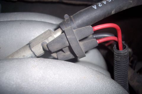 1995 Ford Bronco - A close-up shows two red wires connected to a black rubber boot assembly, which is attached to a metal component on a vehicle's engine. A r…