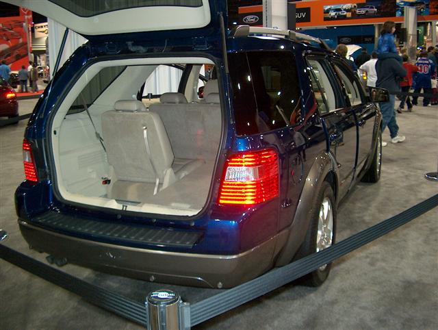 Blue SUV's open tailgate reveals beige interior and folded seats. Rear bumper is dark gray