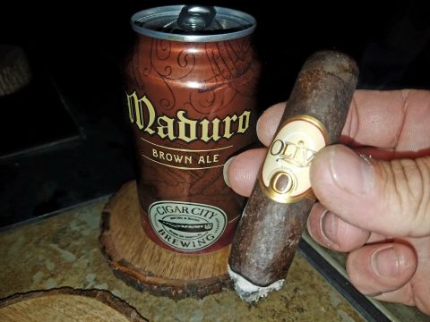 2018 Ford Bronco - A hand holds a cigar next to a can of Maduro Brown Ale. The can is on a wooden coaster.