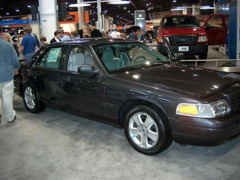2001 Ford Crown Victoria - A dark gray 2001 Ford Crown Victoria sedan is displayed at the Atlanta Auto Show, with a red Ford Ranger pickup truck visible in the backgr…