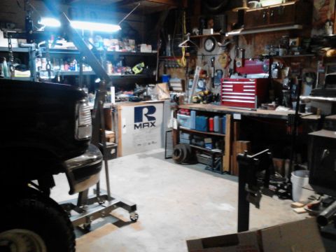 1995 Ford Bronco - A black vehicle, possibly a 1995 Ford Bronco, is parked in a cluttered garage next to an engine hoist. The garage is filled with tools, she…