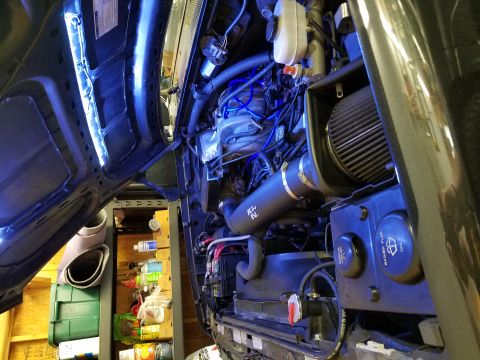 1995 Ford Bronco - The open hood of a vehicle reveals a detailed view of the engine bay, illuminated by blue LED lights. Visible components include an air int…