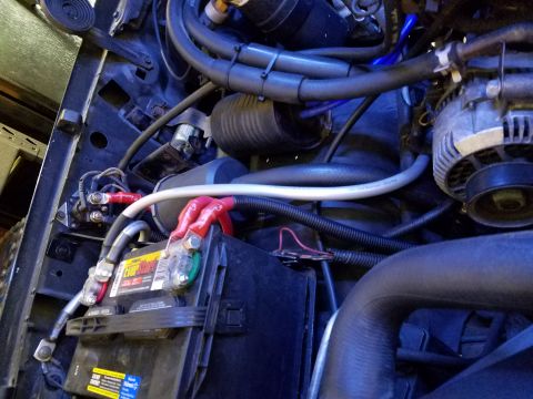 1995 Ford Bronco - The engine bay of a 1995 Ford Bronco shows a close-up of the battery and associated wiring. Red and black cables connect to the battery ter…