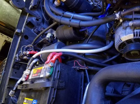 1995 Ford Bronco - The engine bay of a 1995 Ford Bronco shows the battery terminals, starter solenoid, and various hoses and wiring. Red and black battery cab…