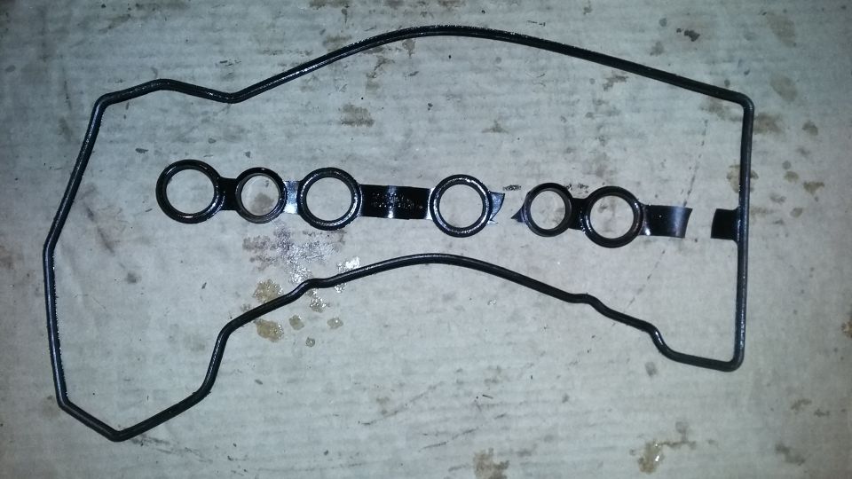Black valve cover gasket with circular cutouts on a concrete surface.