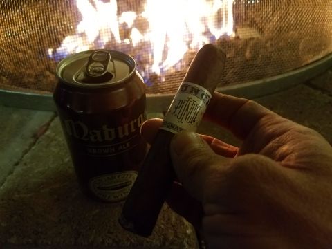 2018 Ford Bronco - A hand holds a cigar with a "Punch" band next to a can of "Maduro Brown Ale" from Cigar City Brewing. A fire burns in the background.