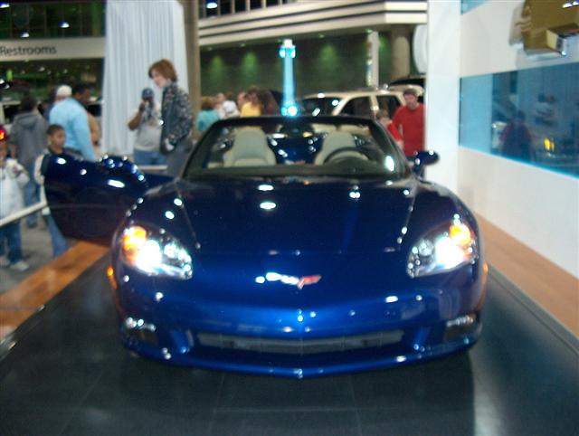 Front view of a blue convertible sports car with doors open, on display indoors