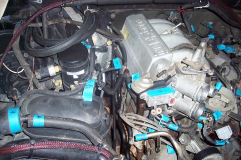 1995 Ford Bronco - A close-up view of an engine bay with various components labeled with blue tape. Several hoses, wires, and parts of the intake manifold are…