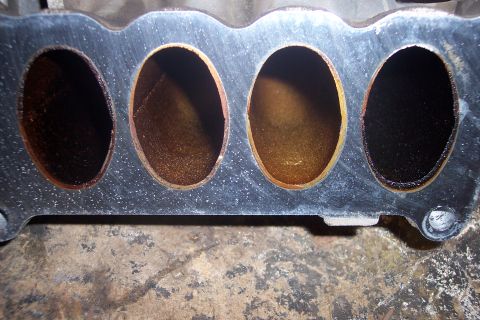 1995 Ford Bronco - A close-up view of the intake manifold ports, showing significant carbon buildup and discoloration within the passages. The gasket surface…