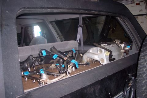 1995 Ford Bronco - The interior cargo area of a black Ford Bronco is filled with engine parts, including intake manifolds and fuel injectors, laid out on the…