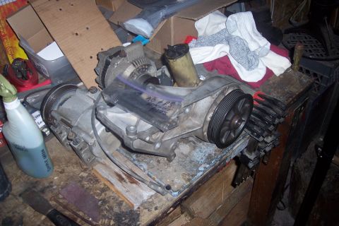 1995 Ford Bronco - A power steering pump and alternator assembly with a pulley is laid out on a workbench. A plastic bag with handwritten text is attached to…
