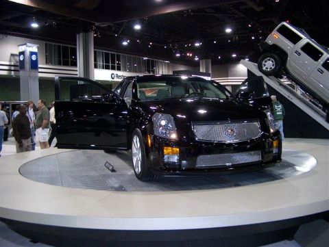 2001 Ford Crown Victoria - A black Cadillac sedan is displayed with its doors open, while a silver Hummer is positioned on a ramp in the background.