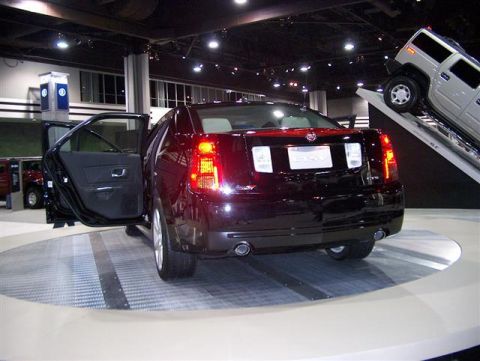 2001 Ford Crown Victoria - A black sedan is displayed with its doors open on a turntable, with a Hummer visible in the background at an auto show.