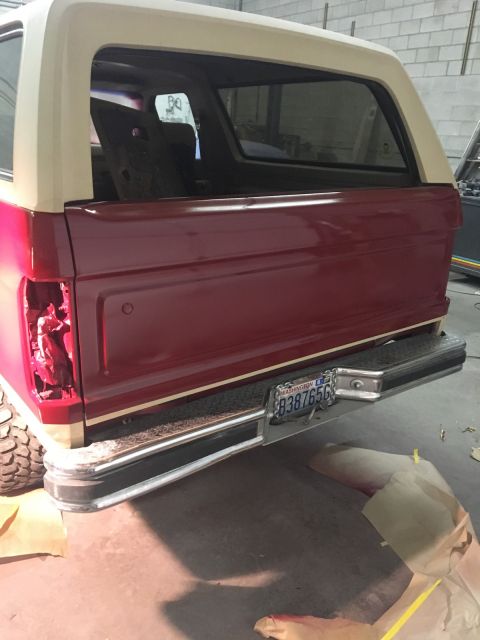 1985 Ford Bronco - The rear passenger side of a dark red and tan Ford Bronco is shown in a garage setting. The vehicle has a Washington license plate and a ch…