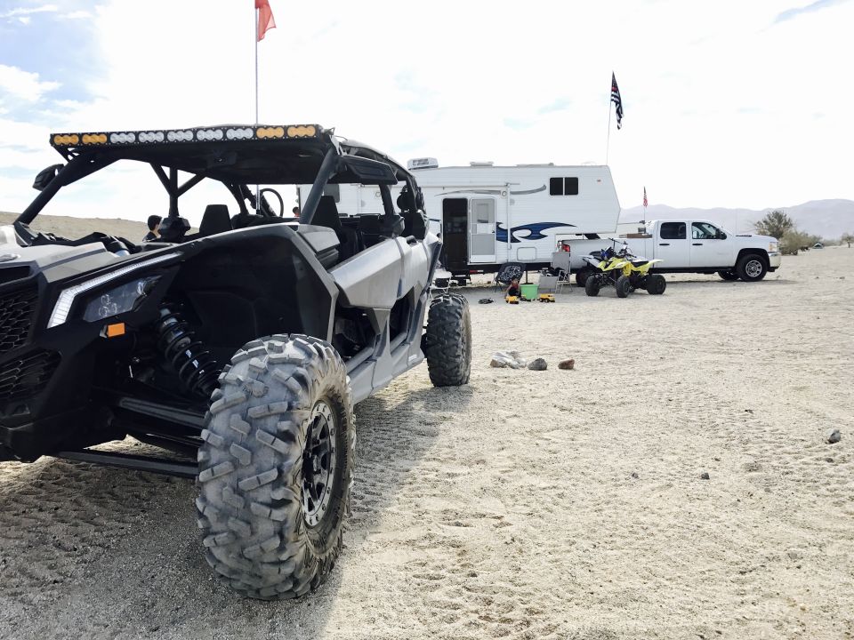 Side-by-side UTV parked in sand, with a trailer and pickup truck behind it