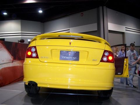 2001 Ford Crown Victoria - A yellow Pontiac GTO is displayed with its rear facing the camera, showing off its distinctive taillights and dual exhaust pipes.