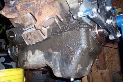 1995 Ford Bronco - A heavily soiled oil pan and engine block are shown, with significant oil leaks and grime covering the metal surfaces. A yellow bucket is v…