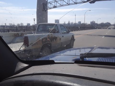 1994 Ford Bronco - A pickup truck is seen from inside another vehicle on a highway, with a city skyline in the background.