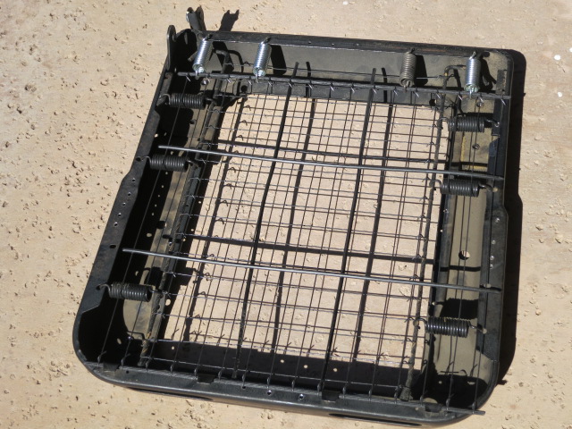 Black seat frame with wire mesh and coil springs on dirt ground