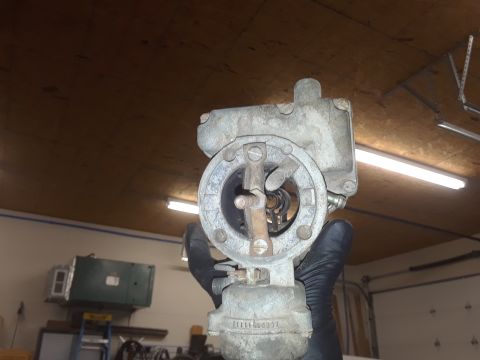1994 Ford Bronco - Gloved hands hold a carburetor, showing internal mechanisms and a visible part number on its base.
