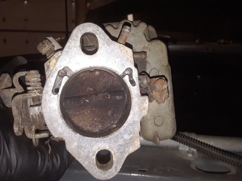 1994 Ford Bronco - Close-up of a carburetor, held by a gloved hand, showing internal components and external linkages.
