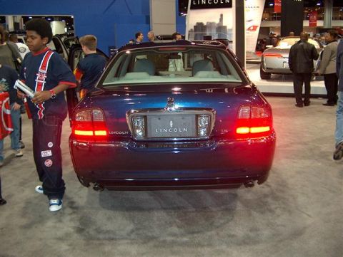 2001 Ford Crown Victoria - Blue Lincoln sedan displayed at an auto show with other vehicles and attendees visible.
