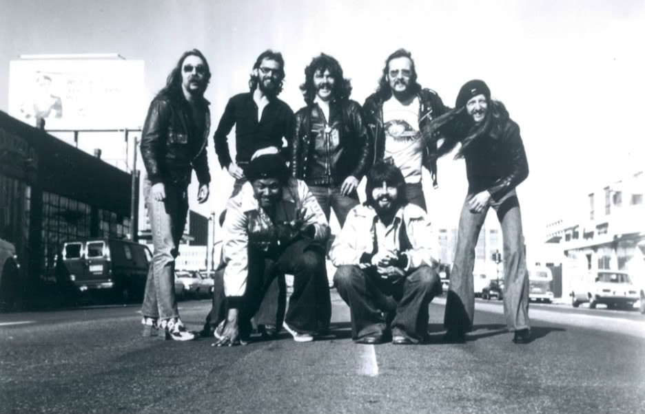Group of men posing on a street with vans and cars in the background