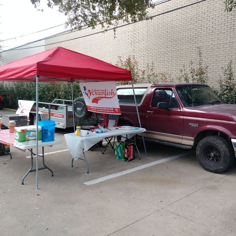 Maroon 1996 Ford Bronco parked next to a red tent with crawfish banner and tables