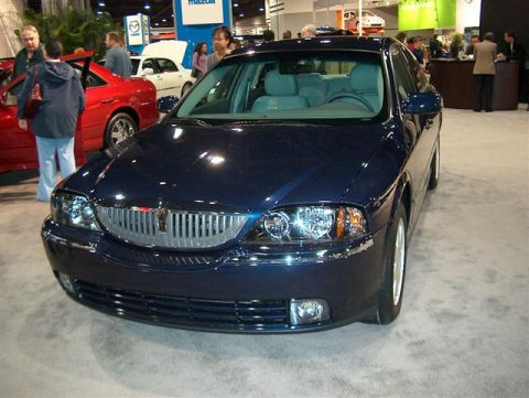 2001 Ford Crown Victoria - A dark blue Lincoln LS sedan is displayed at an auto show, with other vehicles and people in the background.