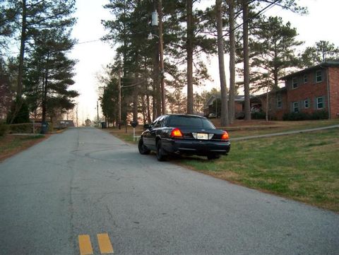 2001 Ford Crown Victoria - A black 2001 Ford Crown Victoria is seen from the rear, parked on the side of a quiet residential street.