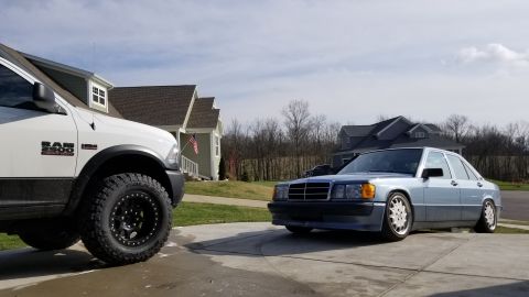 1995 Ford Bronco - A light blue Mercedes-Benz 190E is parked in a driveway next to a white Ram 2500 truck.