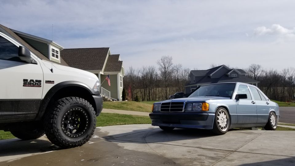 Light blue Mercedes-Benz 190E parked in driveway next to a white Ram 2500 truck