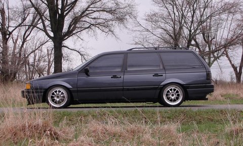 1995 Ford Bronco - A dark gray station wagon is viewed from the side, parked on the side of a road with trees in the background.