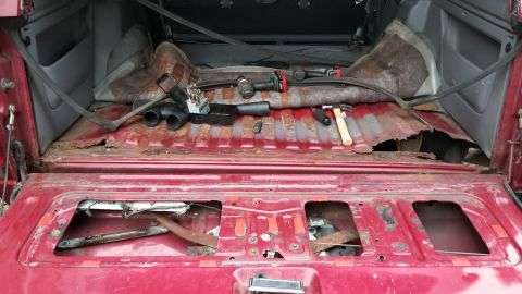 1995 Ford Bronco - The interior cargo space of a red SUV shows significant rust and damage, with tools present.