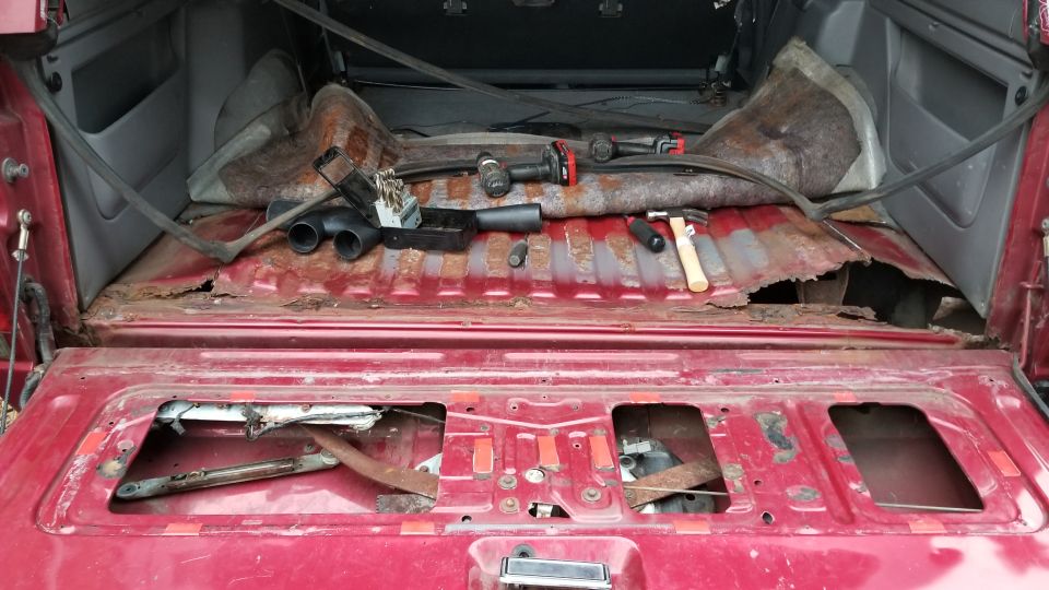 Red SUV's heavily rusted and damaged rear cargo area with tools scattered