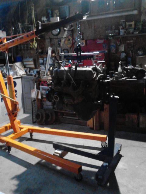 1995 Ford Bronco - An engine is suspended by a hoist and supported by a stand, ready for work in a cluttered garage.