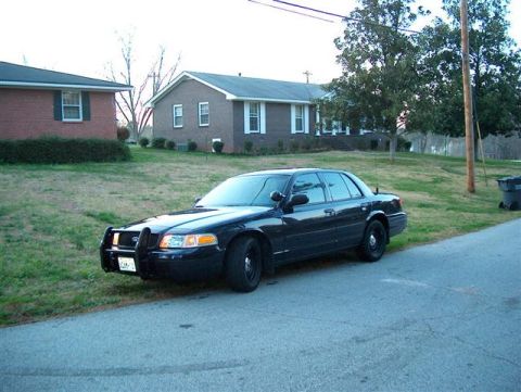 2001 Ford Crown Victoria - A black 2001 Ford Crown Victoria police car is parked on the side of a street in front of houses.