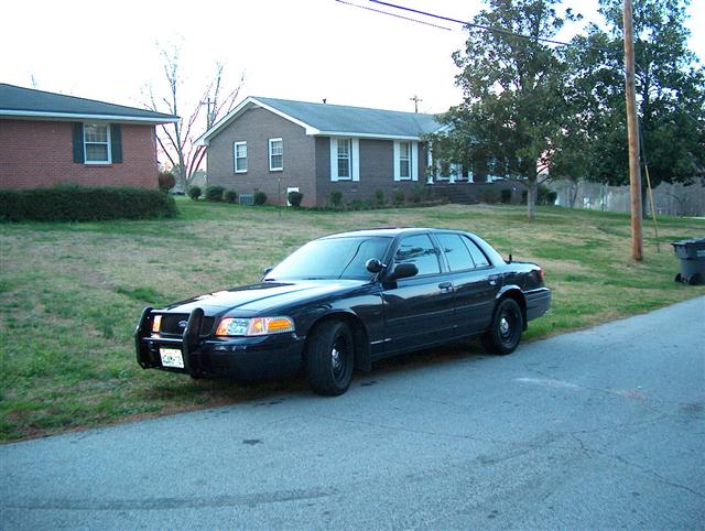 Black Crown Victoria police sedan with push bumper and steel wheels parked on a residential street